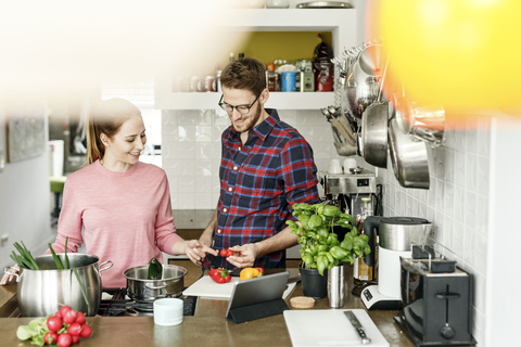 Glückliches junges Paar mit Tablet kochen zusammen in der Küche, lizenzfreies Stockfoto