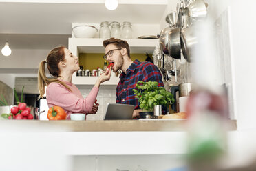 Junges Paar mit Tablet, das in der Küche Gemüse probiert - PESF00844