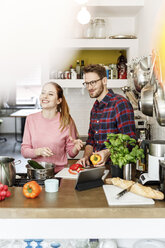 Happy young couple with tablet cooking together in kitchen - PESF00845