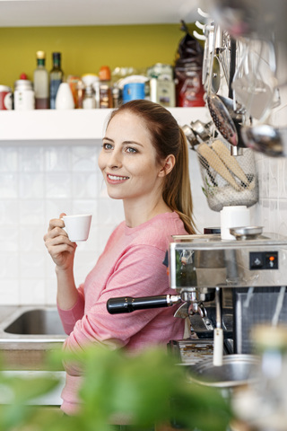 Lächelnde junge Frau mit einer Tasse Espresso in der Küche zu Hause, lizenzfreies Stockfoto