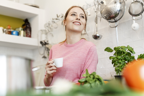 Lächelnde junge Frau mit einer Tasse Espresso in der Küche zu Hause, lizenzfreies Stockfoto