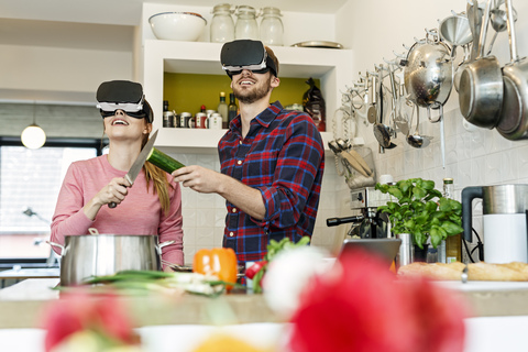 Glückliches junges Paar mit VR-Brille beim gemeinsamen Kochen in der Küche, lizenzfreies Stockfoto