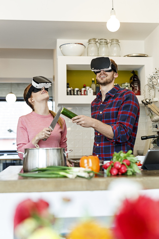 Glückliches junges Paar mit VR-Brille beim gemeinsamen Kochen in der Küche, lizenzfreies Stockfoto