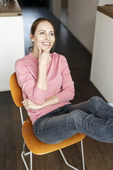 Porträt einer lächelnden jungen Frau, die zu Hause auf einem Holzstuhl sitzt - PESF00859
