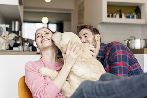 Happy young couple cuddling with dog at home stock photo