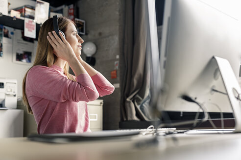 Smiling young woman wearing headphones at desk at home - PESF00875