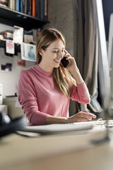 Lächelnde junge Frau am Telefon am Schreibtisch zu Hause - PESF00878