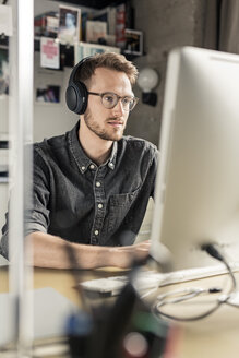 Junger Mann mit Kopfhörern bei der Arbeit am Computer am Schreibtisch zu Hause - PESF00883