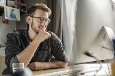 Lächelnder junger Mann bei der Arbeit am Computer am Schreibtisch zu Hause - PESF00886