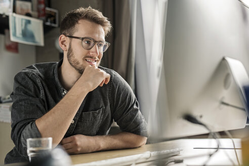 Lächelnder junger Mann bei der Arbeit am Computer am Schreibtisch zu Hause - PESF00886