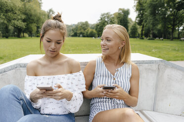 Zwei glückliche junge Frauen mit Handys in einem Skatepark - KNSF03050