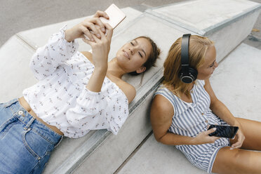 Two young women with cell phones and headphones in a skatepark - KNSF03060