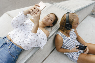 Zwei junge Frauen mit Handys und Kopfhörern in einem Skatepark - KNSF03060