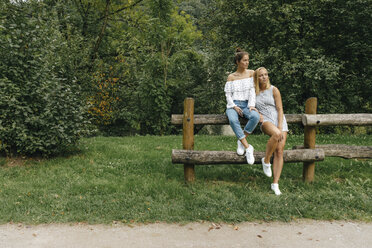 Zwei junge Frauen sitzen auf einem Zaun in einem Park - KNSF03076