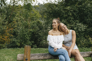 Zwei glückliche junge Frauen sitzen auf einem Zaun in einem Park - KNSF03077