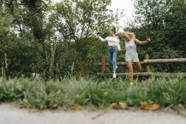 Zwei glückliche junge Frauen springen vom Zaun in einem Park - KNSF03078