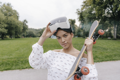 Porträt einer jungen Frau mit VR-Brille, die ein Skateboard hält, lizenzfreies Stockfoto