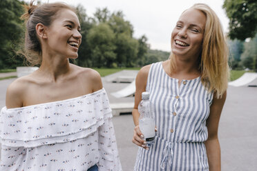 Zwei lachende junge Frauen mit einer Wasserflasche im Freien - KNSF03083