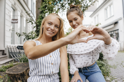 Zwei lächelnde junge Frauen, die mit ihren Händen ein Herz in der Stadt formen, lizenzfreies Stockfoto