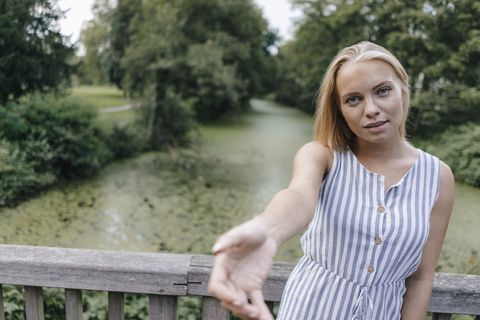 Portrait of young woman standing on a bridge reaching out her hand stock photo