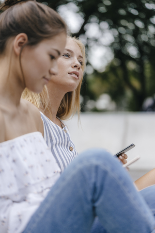 Junge Frau mit Freund, der sich hinsetzt und ein Mobiltelefon hält, lizenzfreies Stockfoto