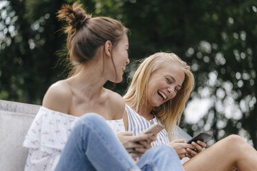 Two laughing young women with cell phones outdoors - KNSF03108