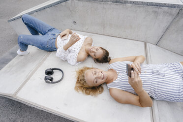 Two happy young women with cell phone and headphones in a skatepark - KNSF03113