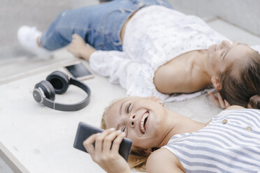 Zwei glückliche junge Frauen mit Handy und Kopfhörern in einem Skatepark - KNSF03114