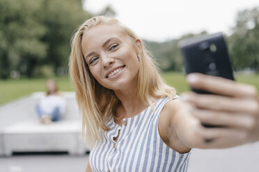 Porträt einer lächelnden jungen Frau, die ein Selfie in einem Skatepark macht - KNSF03119