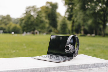 Laptop und Kopfhörer an einer Wand in einem Park - KNSF03127