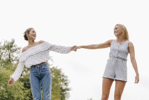 Zwei glückliche junge Frauen halten sich im Freien die Hände - KNSF03128