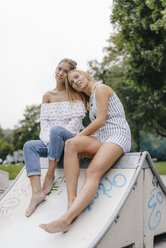 Junge Frau sitzt im Skatepark und stützt sich auf die Schulter einer Freundin - KNSF03135