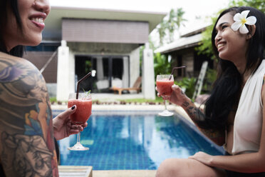 Two happy women drinking cocktails at swimming pool - IGGF00232