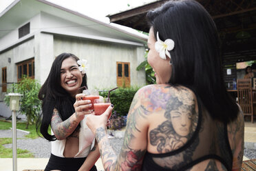 Two happy women toasting with cocktails in garden - IGGF00235