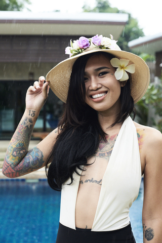 Portrait of smiling woman with flower in her hair wearing a straw hat at a swimming pool stock photo