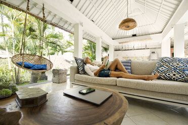 Attractive senior woman relaxing on couch, reading a book - SBOF00934