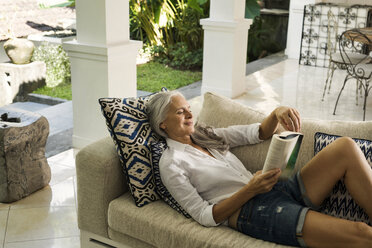 Attractive senior woman relaxing on couch, reading a book - SBOF00935