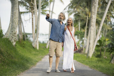 Handsome senior couple strolling through tropical landscape with palm trees - SBOF00958