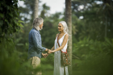 Zärtliches älteres Paar, das sich in einer tropischen Landschaft mit Palmen an den Händen hält - SBOF00959