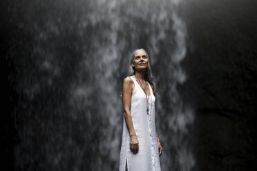 Schöne ältere Frau steht vor einem tropischen Wasserfall - SBOF00966
