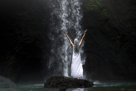 Schöne ältere Frau steht vor einem tropischen Wasserfall, lizenzfreies Stockfoto