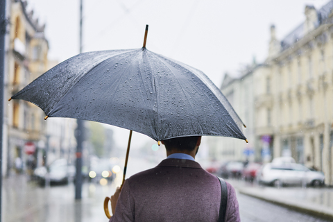 Rückansicht eines Geschäftsmannes in der Stadt mit Regenschirm an einem regnerischen Tag, lizenzfreies Stockfoto
