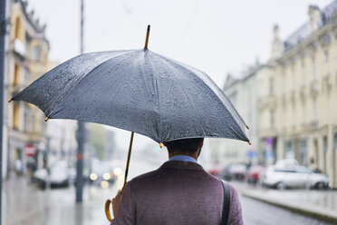 Rückansicht eines Geschäftsmannes in der Stadt mit Regenschirm an einem regnerischen Tag - BSZF00101