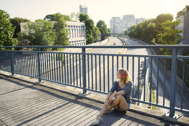 Junge Frau sitzt auf einer Brücke und hört Musik mit Kopfhörern - KNSF03141