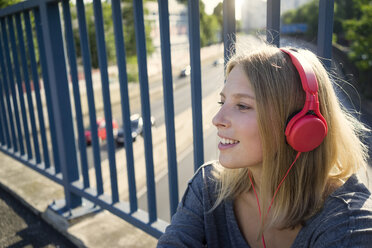 Porträt einer lächelnden jungen Frau, die mit Kopfhörern Musik hört - KNSF03146