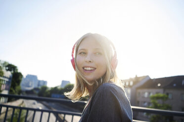 Portrait of smiling young woman at backlight listening music with headphones - KNSF03149
