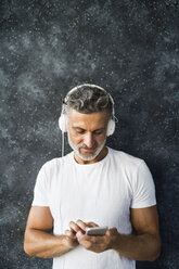 Porträt eines reifen Mannes, der ein Smartphone benutzt und Kopfhörer trägt - HAPF02457