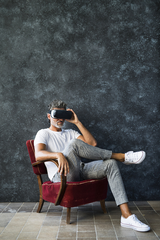 Älterer Mann schaut durch eine VR-Brille, sitzt im Sessel, lizenzfreies Stockfoto