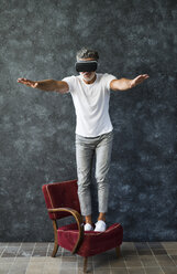 Mature man looking through VR glasses, balancing on armchair - HAPF02471