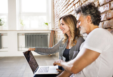 Businessman and woman sitting in a loft, using laptop, founding a start-up company - HAPF02476